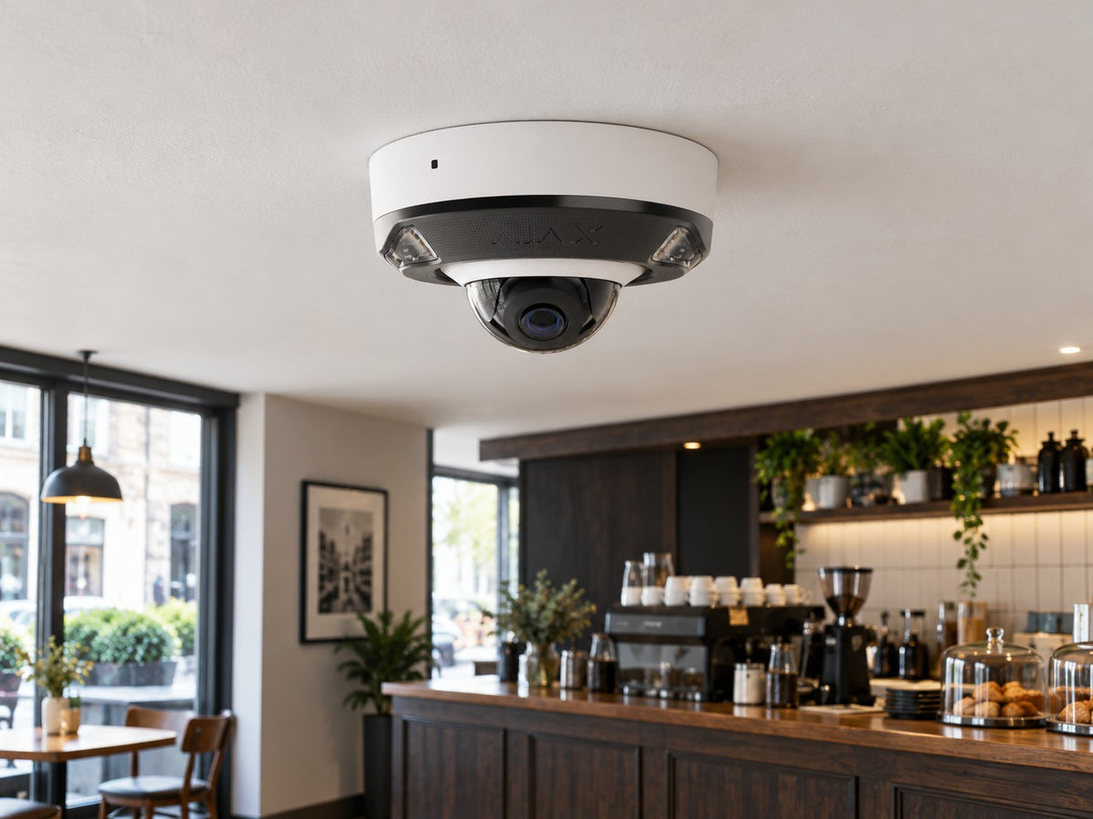 Ajax DomeCam Mini HL • 5MP 4mm • White installed in small British cafe interior, pale ceiling and dark timber counter.