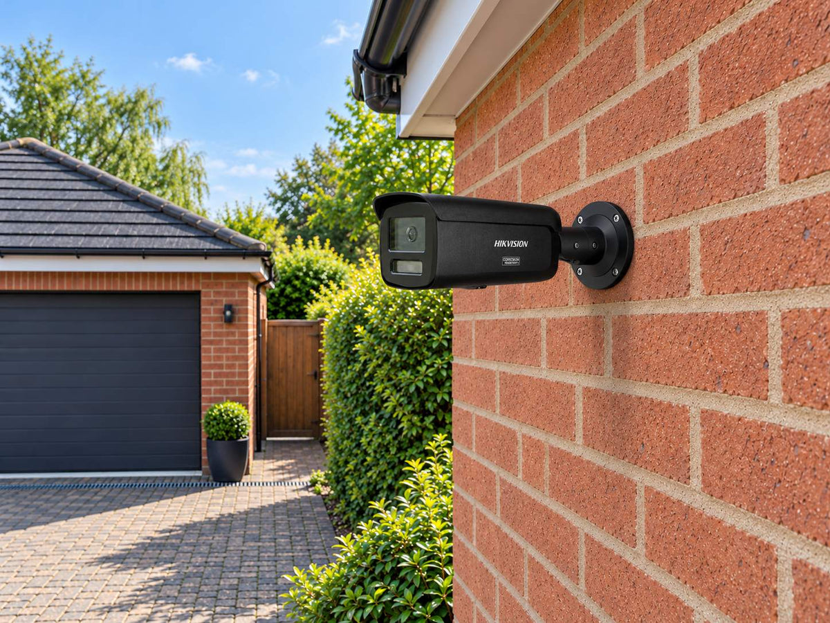 Hikvision DS-2CD2T87G3-LIY • Black installed in A UK red-brick detached home beside its garage, daylight and a paved driveway below.
