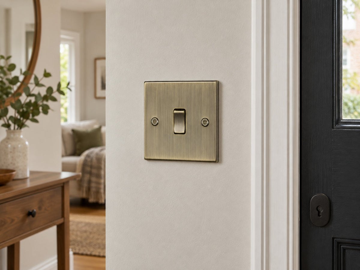 Knightsbridge CS12AB antique brass intermediate switch installed in a UK living-room wall beside an entrance, with neutral paint.