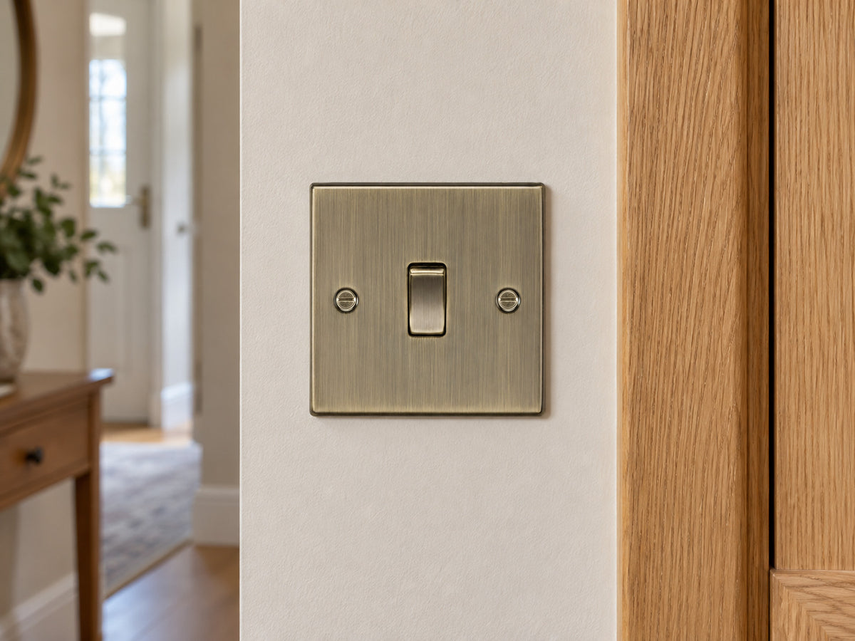 Knightsbridge CS12AB antique brass intermediate switch installed in a UK hallway wall beside an oak door frame.