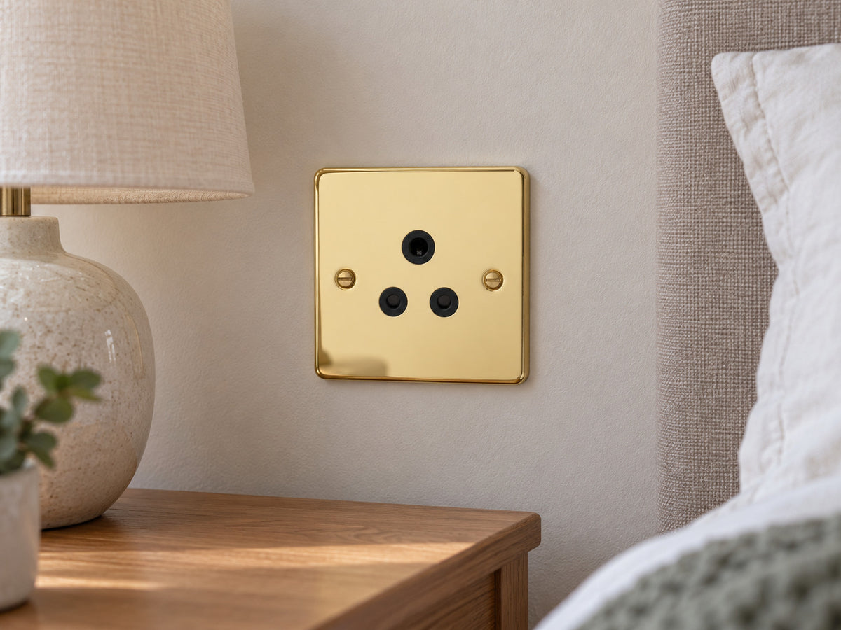 Knightsbridge FP5APB polished brass lighting socket installed in a dry UK bedroom wall near an unconnected bedside lamp.