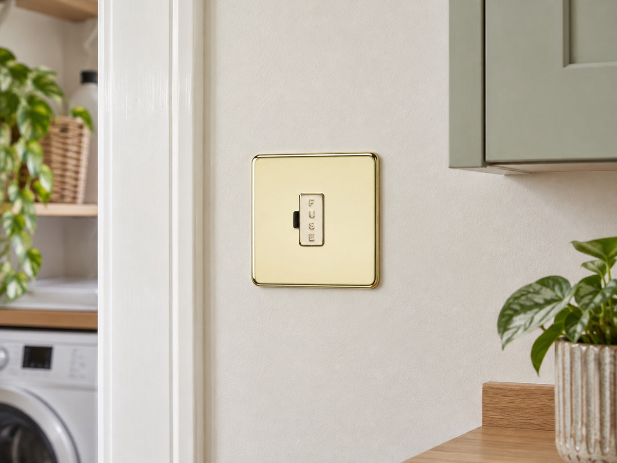 Knightsbridge SF6000PB polished brass fused spur installed on a dry UK utility-room wall near a cupboard, away from water and heat.