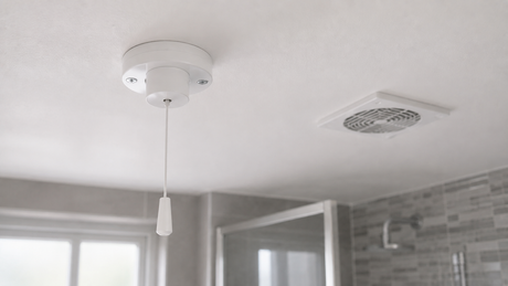 White three-pole pull-cord fan isolator switch on a UK bathroom ceiling beside an extractor fan grille