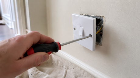 Removing the faceplate of a UK light switch with a screwdriver to replace it