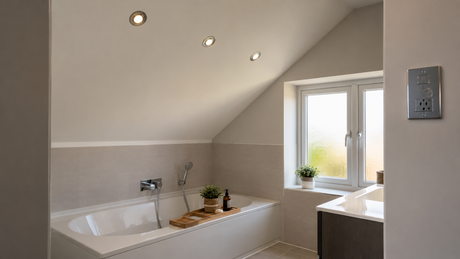 Modern British bathroom with a white bath under a sloped ceiling and three recessed chrome-bezel downlights in a row