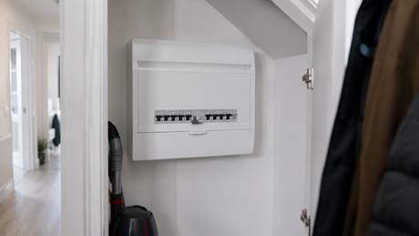Modern UK consumer unit with the cover on, mounted in a white-painted under-stairs cupboard with one switch in the down position