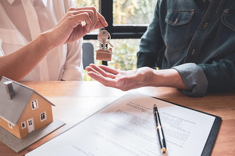 Midsection of agent giving house key to man on table