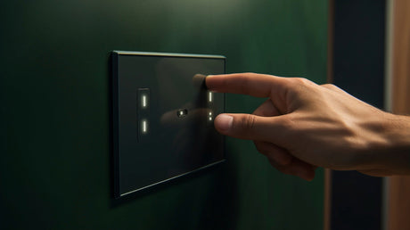 A hand pressing buttons on a lighting control panel on a dark green wall inside a home