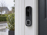 Ajax DoorBell Graphite shown at a white entrance frame.