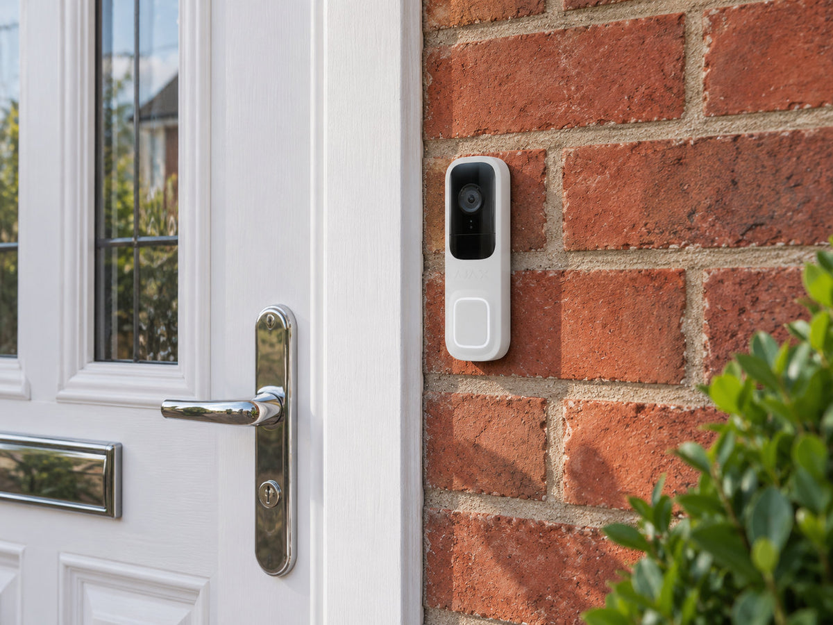 Ajax DoorBell white mounted on red brick beside a white front door.