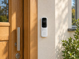 Ajax DoorBell white mounted on a rendered wall beside an oak front door.