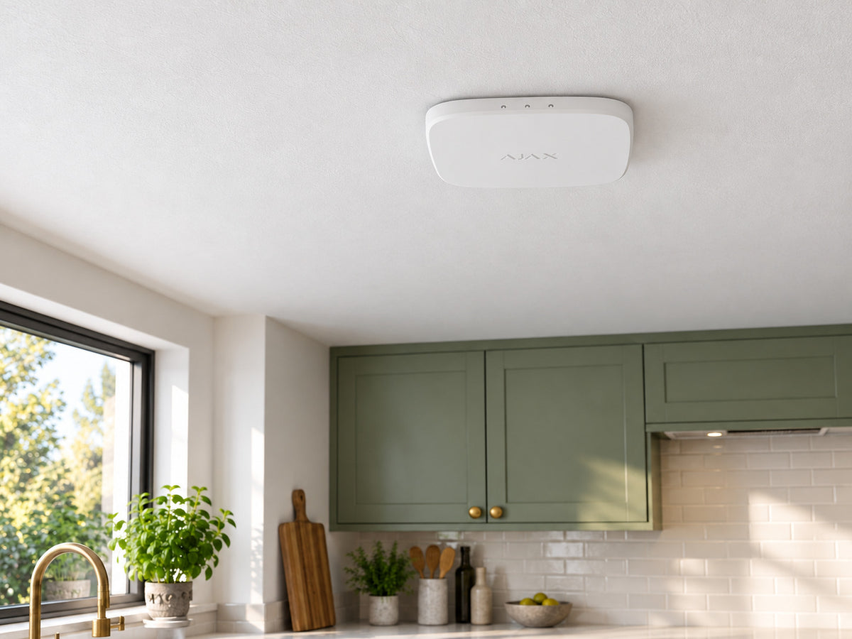 White Ajax FireProtect 2 AC Heat/CO alarm mounted flat against a kitchen ceiling above green cabinets.