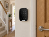 Ajax KeyPad black mounted on a hallway wall beside a timber door.