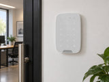 Ajax KeyPad Fibra White shown at a wall beside a door.
