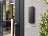 Ajax Superior KeyPad Outdoor Fibra Graphite mounted on a stone wall beside an entrance.