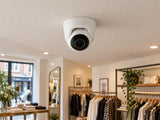 Ajax TurretCam • 8MP 4mm • White installed in British boutique clothing shop interior, warm off-white ceiling.