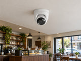 Ajax TurretCam HL • 8MP 4mm • White installed in small British cafe interior, pale ceiling and dark timber counter.