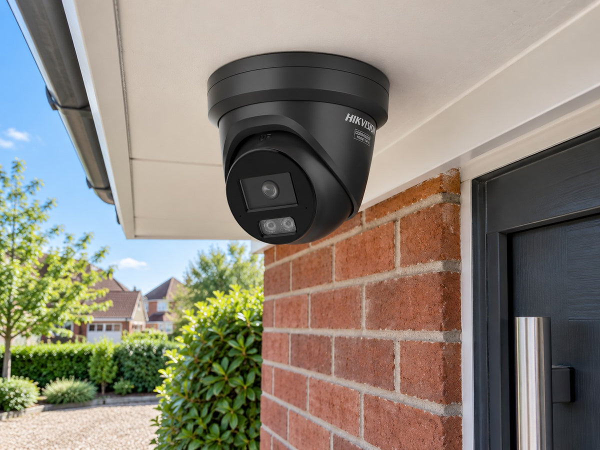 Hikvision DS-2CD2346G3-IZ2UY • Black installed in A UK home entrance beneath a white horizontal canopy, red brick wall and planted driveway below.