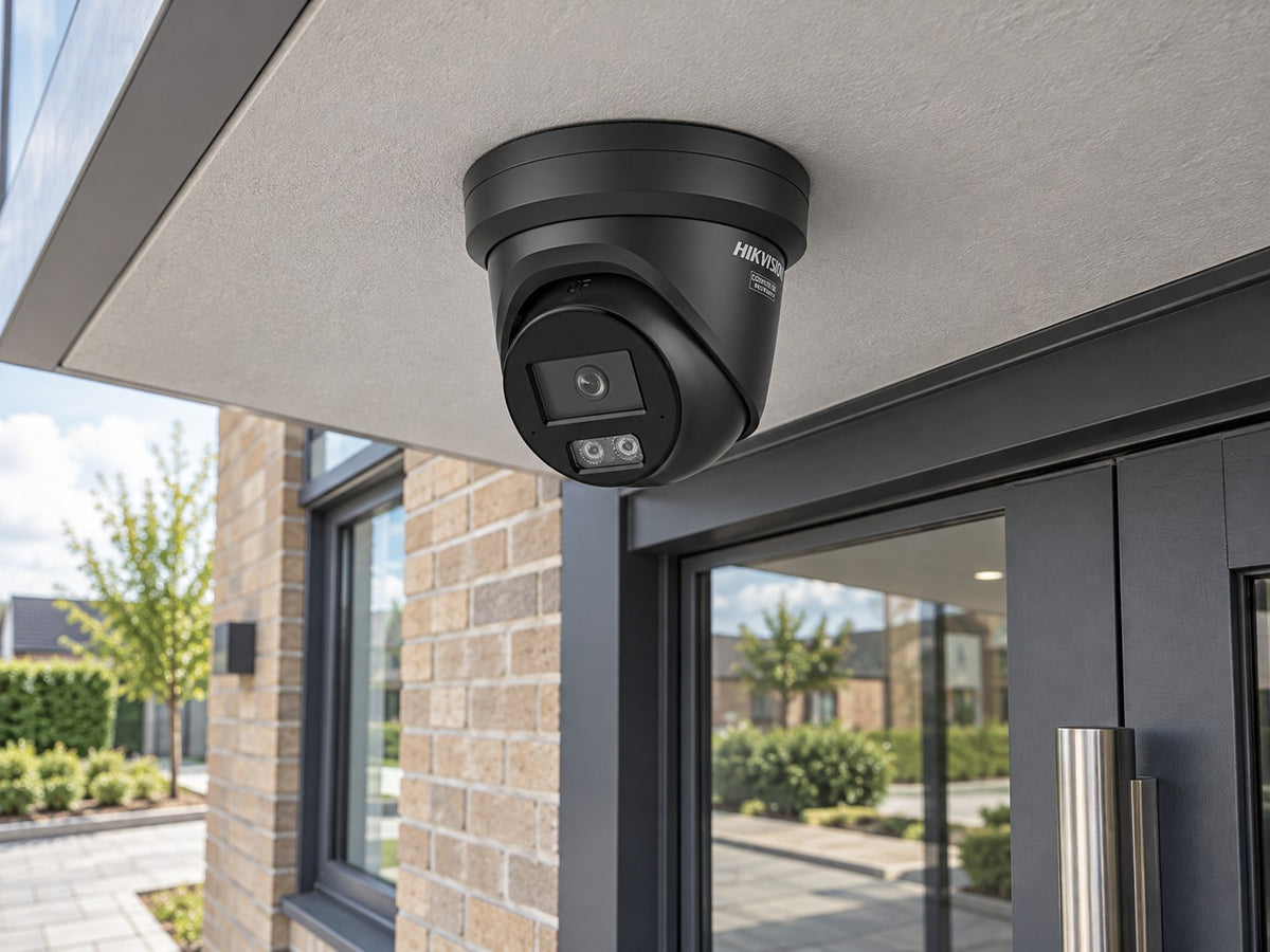 Hikvision DS-2CD2346G3-IZ2UY • Black installed in A UK small business doorway beneath a pale grey flat soffit, dark framed entrance and paved courtyard below.