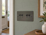 Knightsbridge FP4100GM gunmetal light switch mounted on the wall in a UK living-room entrance wall with muted sage paint.