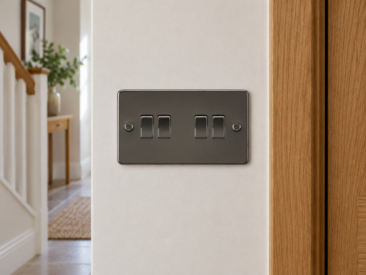 Knightsbridge FP4100GM gunmetal light switch mounted on the wall in a UK hallway wall beside an oak door frame.