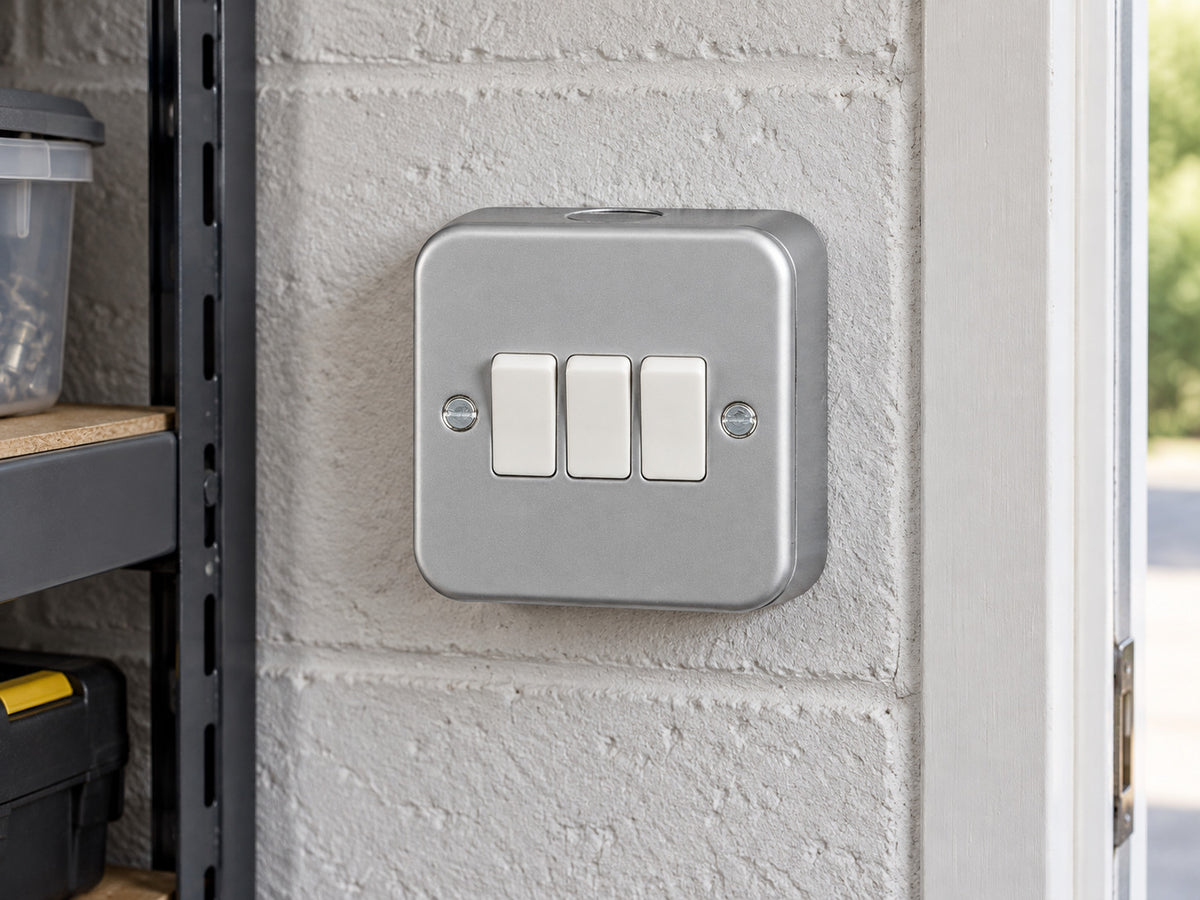 Knightsbridge M4000 powder-coated silver/grey light switch mounted on the wall in a dry garage workshop wall with painted masonry.