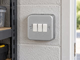 Knightsbridge M4000 powder-coated silver/grey light switch mounted on the wall in a dry garage workshop wall with painted masonry.