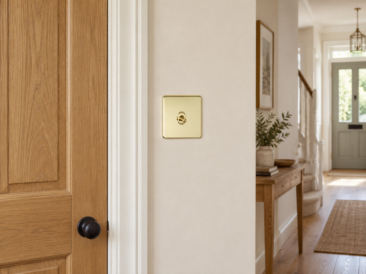 Knightsbridge SF1TOGPB polished brass toggle switch fitted flush in UK hallway beside a timber doorway.