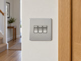 Knightsbridge SF4000BC brushed chrome light switch installed in a UK hallway wall beside an oak door frame.