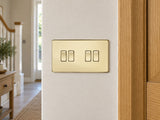 Knightsbridge SF4100PB polished brass light switch installed on a UK hallway wall beside an oak door frame.